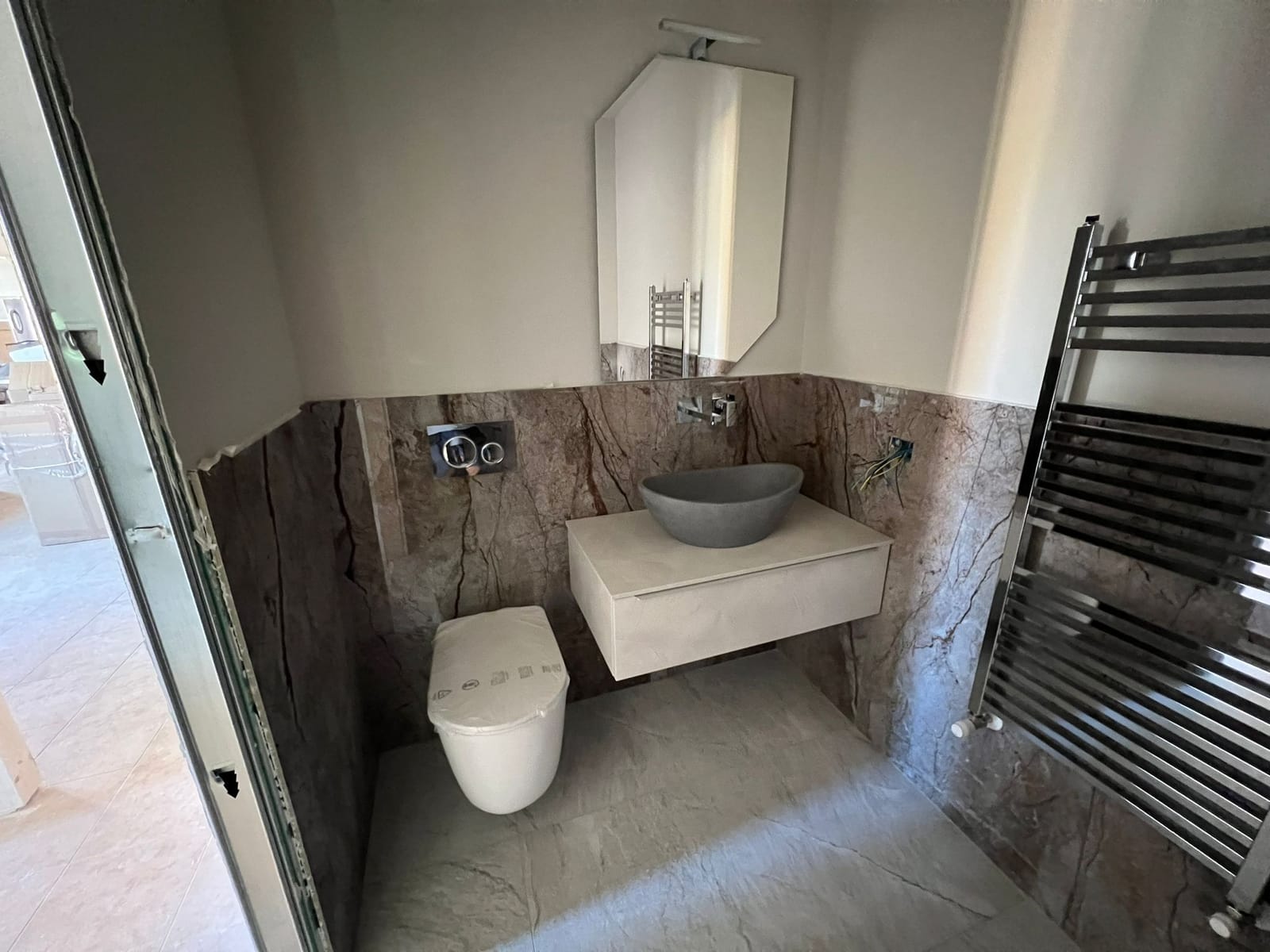 Vista frontale del bagno in lastre effetto marmo bruno con specchio sagomato