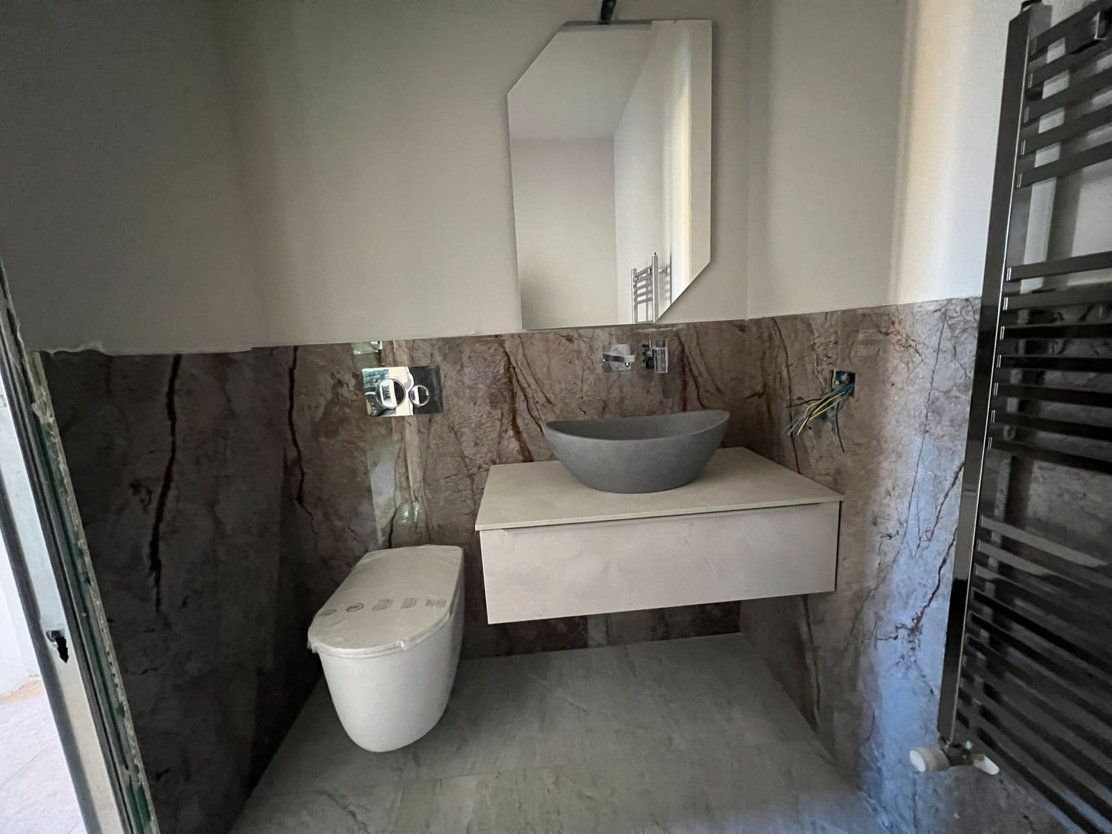 Bagno con grandi lastre effetto marmo bruno, mobile sospeso e lavabo in pietra grigia
