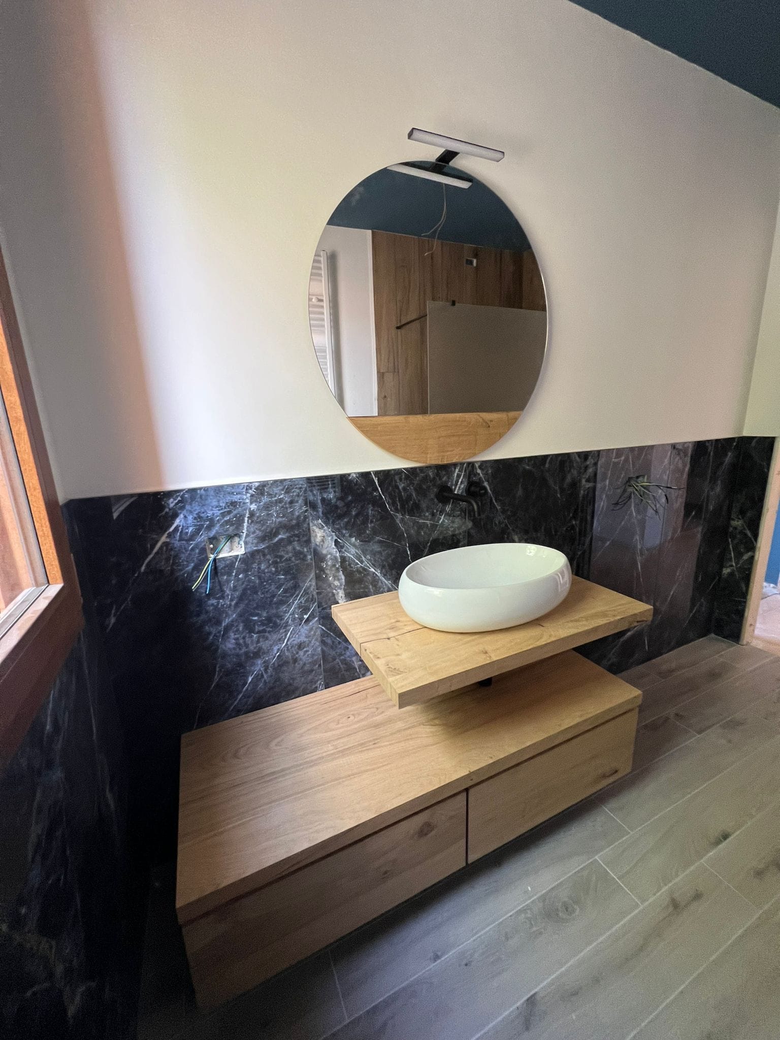 Bagno con rivestimento effetto marmo nero, mobile in rovere e lavabo da appoggio