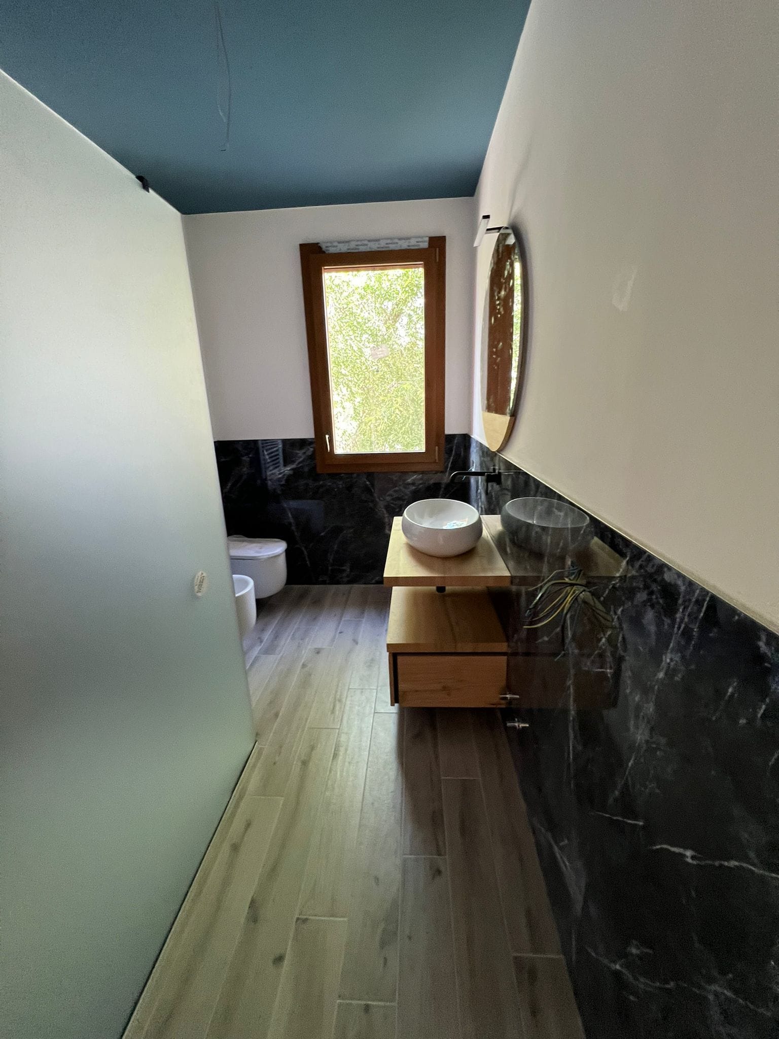 Bagno lungo con pavimento effetto legno, soffitto colorato e finestra in fondo
