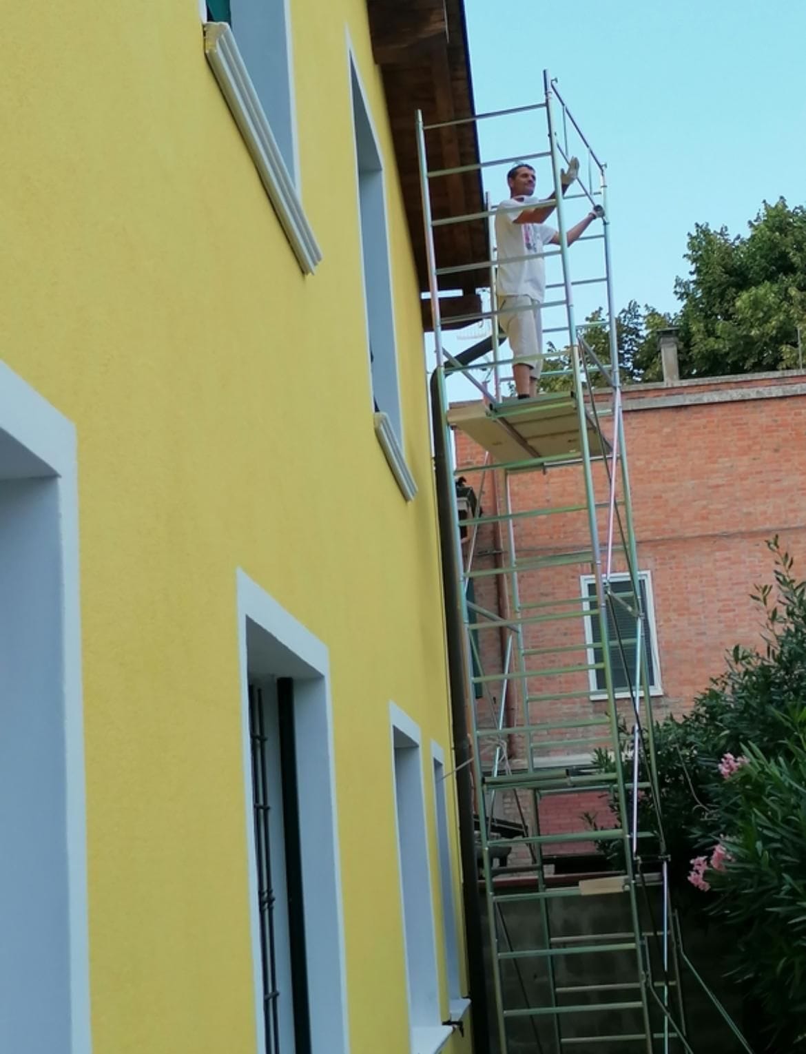 Facciata tinteggiata in giallo con cornici chiare alle finestre, lavori sul ponteggio