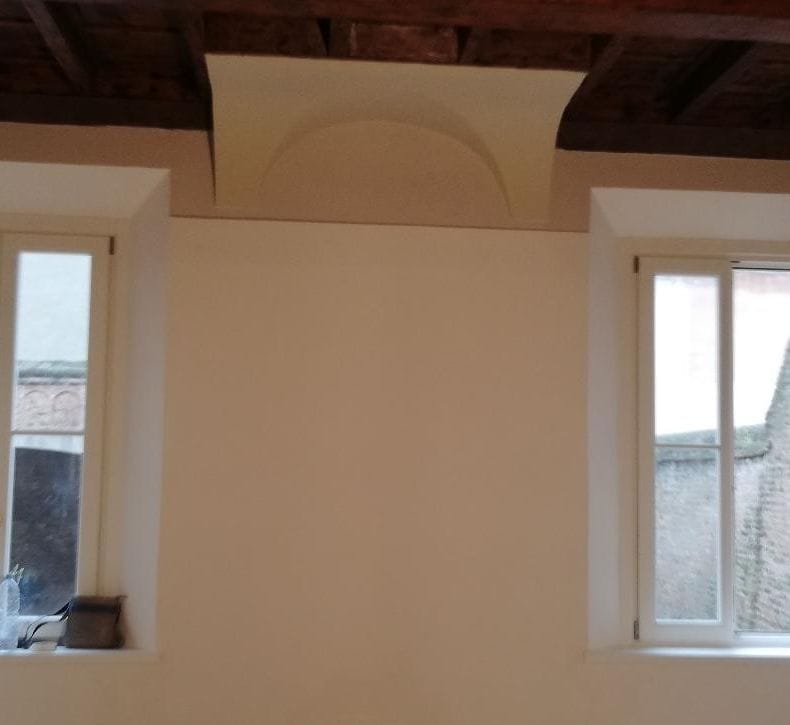 Stanza con soffitto a travi in legno, volta ricostruita tra le finestre e pareti rasate