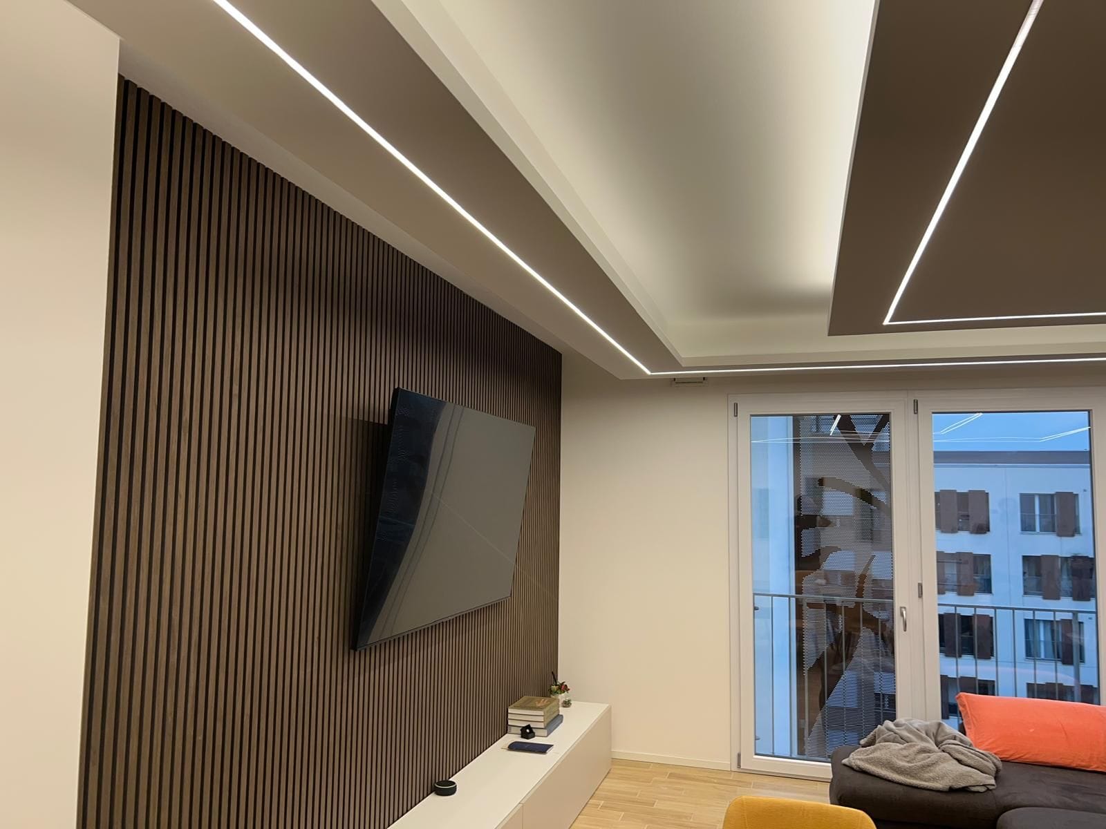 Soggiorno con controsoffitto in cartongesso a gradoni, tagli di luce LED e parete in doghe di legno